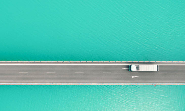 Drone view following big truck from above driving on bridge crossing blue lake in the Pyrenees mountains.